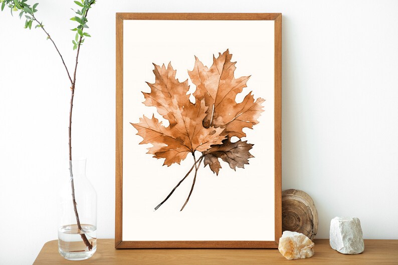 May include: A framed watercolour painting of two brown maple leaves on a white background.