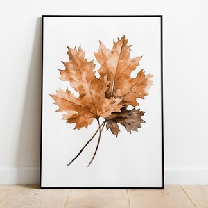 May include: A framed watercolour painting of two brown maple leaves on a white background.