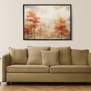 May include: A framed watercolor painting of a foggy forest scene with orange and red trees. The painting is hanging on a beige wall above a brown couch.