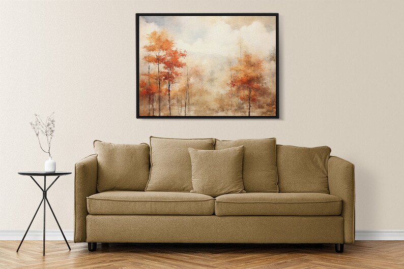 May include: A framed watercolor painting of a foggy forest scene with orange and red trees. The painting is hanging on a beige wall above a brown couch.