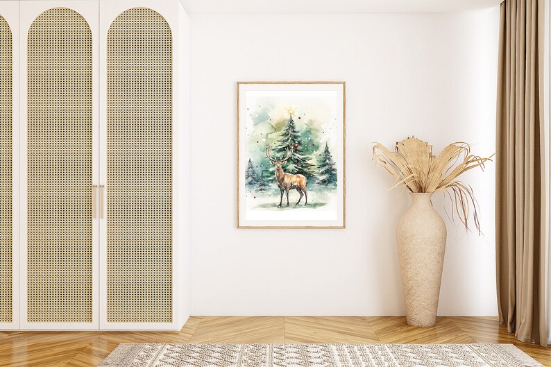 以下が含まれることがあります： 雪の降る森にいる鹿の額装された水彩画。アートワークは明るい木製のフレームに入っています。シーンは、木のてっぺんに星がある冬の風景です。