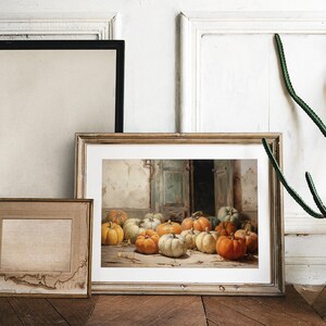Puede incluir: Una pintura enmarcada que representa una naturaleza muerta con una colecci&oacute;n de calabazas en varios tonos de naranja, amarillo y blanco. Las calabazas est&aacute;n dispuestas en un suelo de madera frente a una puerta con una puerta verde descolorida.