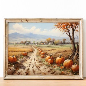 May include: A framed landscape painting shows an autumnal scene with a dirt track lined with pumpkins. The track leads to a village with a church and houses, set against a backdrop of mountains and a blue sky. The painting is in a rustic, wooden frame.