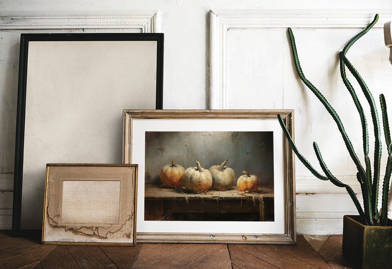 May include: A framed painting of a still life with four pumpkins on a wooden table. The pumpkins are various shades of orange and white. The painting is in a light wood frame and is hanging on a white wall.