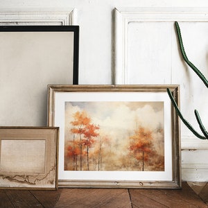 May include: Three framed pictures on a white wall with a potted cactus plant. The center picture is a watercolor painting of a forest scene with orange and brown trees. The picture on the left is a blank canvas. The picture on the right is a blank canvas.