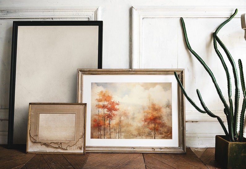 May include: Three framed pictures on a white wall with a potted cactus plant. The center picture is a watercolor painting of a forest scene with orange and brown trees. The picture on the left is a blank canvas. The picture on the right is a blank canvas.