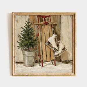 Op de afbeelding: Een ingelijst schilderij met een kleine groene dennenboom in een gegalvaniseerde metalen emmer, een houten slee met rode metalen glijders en een paar witte schaatsen die aan de slee hangen, tegen een lichte houten wand.