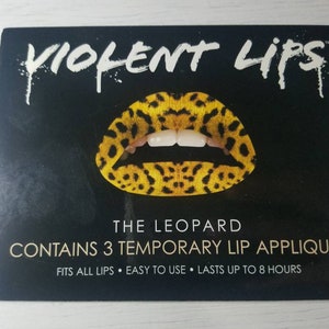 May include: A black and white package with the text "VIOLENT LIPS" in white. The package features a leopard print temporary lip appliqué. The text "THE LEOPARD" is printed below the appliqué. The text "CONTAINS 3 TEMPORARY LIP APPLIQUÉS" is printed below the text "THE LEOPARD". The text "FITS ALL LIPS EASY TO USE LASTS UP TO 8 HOURS" is printed below the text "CONTAINS 3 TEMPORARY LIP APPLIQUÉS".