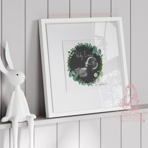 May include: A white frame containing a black and white ultrasound image of a baby, encircled by a green eucalyptus wreath. The text 'Baby Evans' and the date '1st September 2023' are written beneath the image.