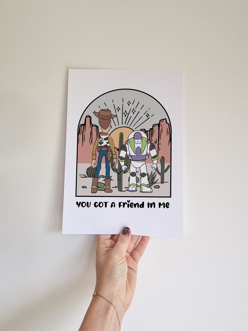 May include: A print featuring a cartoon illustration of Woody and Buzz Lightyear from Toy Story standing in a desert landscape with the text "You got a friend in me".