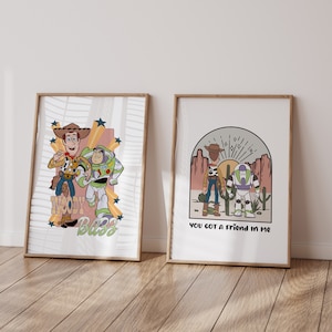 May include: Two framed prints featuring illustrations of Woody and Buzz Lightyear from the Toy Story franchise. The first print shows Woody and Buzz standing together with the text "Woody Buzz" below them. The second print shows Woody and Buzz standing in a desert landscape with the text "You got a friend in me" below them.
