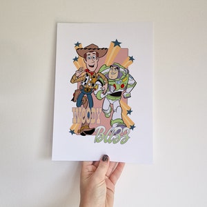 May include: A retro-style print featuring Woody and Buzz Lightyear from Toy Story. The characters are depicted in a cartoon style with a yellow, orange, and pink background. The text "Woody Buzz" is written in a stylized font.