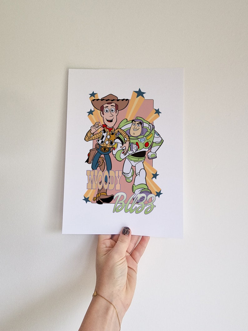 May include: A retro-style print featuring Woody and Buzz Lightyear from Toy Story. The characters are depicted in a cartoon style with a yellow, orange, and pink background. The text "Woody Buzz" is written in a stylized font.