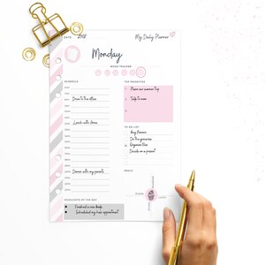 May include: A pink and gray daily planner with a pink heart and the word "Monday" at the top. The planner has sections for schedule, mood tracker, top priorities, to do list, and meals. It also has a section for highlights of the day.