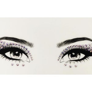 Puede incluir: Una hoja de pegatinas de maquillaje para ojos con dos pares de ojos rodeados de diamantes de imitación. Los diamantes de imitación son iridiscentes y tienen un tono morado.