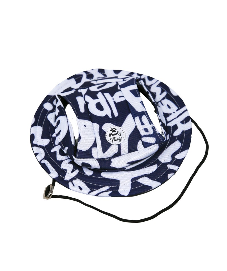May include: A blue and white dog hat with a black strap and a small white circle with the text "Pawly Things" and a paw print.