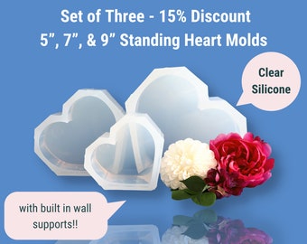 May include: Set of three clear silicone heart molds, 5", 7", and 9" in size, with built-in wall supports. The image also shows white and red flowers against a blue background. The molds are designed for standing.