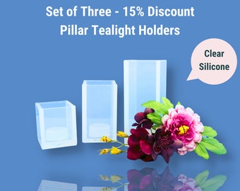 May include: Set of three clear silicone pillar tealight holders. The holders are in different sizes and are arranged in a row from smallest to largest. The holders are on a blue background with a flower arrangement in front of them. The text "Clear Silicone" is in a speech bubble above the holders.