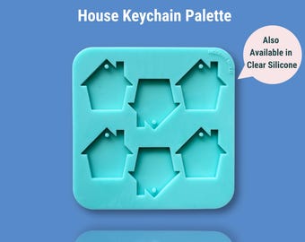 May include: A turquoise silicone mold for making house-shaped keychains. The mold has six cavities, each shaped like a simple house with a small hole for a keychain ring. The text "Also Available in Clear Silicone" is written in a speech bubble in the upper right corner of the image.