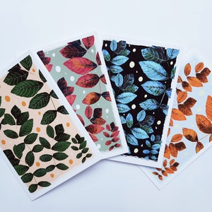 May include: Four cards with different patterns of leaves. The cards are all white with a light background color and a pattern of leaves in different colors. The leaves are all different shapes and sizes. The cards are arranged in a fan shape.