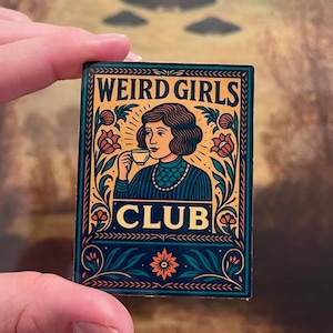 May include: A rectangular sticker featuring a dark teal border with orange floral accents. The center displays a person with dark hair drinking from a small cup, surrounded by the text WEIRD GIRLS CLUB in bold, dark lettering against a light orange background.
