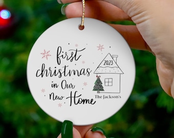 May include: White ceramic Christmas ornament with the text "first christmas in our new home" and a small house illustration with the year 2023. The text "The Jackson's" is also included.