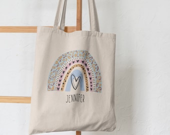 May include: A beige canvas tote bag with a rainbow design featuring a heart and leopard print accents. The bag has the name "Jennifer" printed below the rainbow.