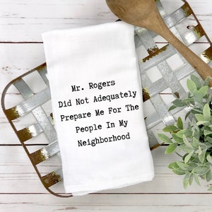 Peut inclure: Une serviette de cuisine blanche avec le texte "Mr. Rogers Did Not Adequately Prepare Me For The People In My Neighborhood" imprimé en noir.