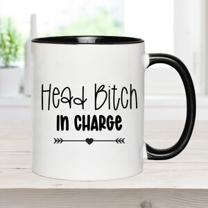 May include: White ceramic mug with a black rim and handle. The mug has black text that reads "Head Bitch in Charge" with arrows and a heart.