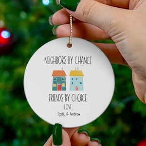 May include: White ceramic Christmas ornament with a colorful illustration of two houses and the text "Neighbors by chance, friends by choice, love. Jodi & Andrew".