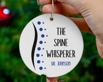 Może przedstawiać: Biała, okrągła ozdoba choinkowa z niebieskim obrazkiem kręgosłupa i tekstem "The Spine Whisperer Dr. Johnson".