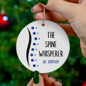 May include: White round Christmas ornament with a blue spine illustration and the text "The Spine Whisperer Dr. Johnson".