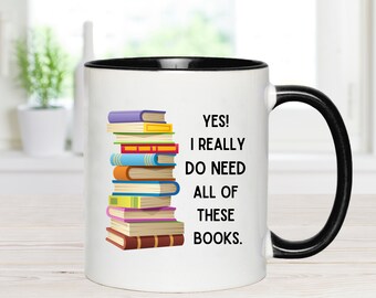 May include: White coffee mug with a black rim and handle. The mug features a stack of colorful books and the text "YES! I REALLY DO NEED ALL OF THESE BOOKS."