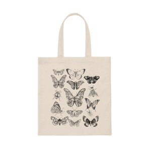 Puede incluir: Una bolsa de lona natural con un estampado en blanco y negro de varias mariposas e insectos. El estampado presenta una variedad de especies de mariposas, incluyendo monarcas, swallowtails y damas pintadas.