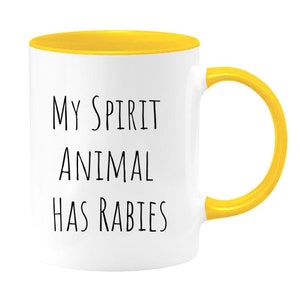 May include: White ceramic mug with a yellow rim and handle. The mug has black text that reads "My Spirit Animal Has Rabies."