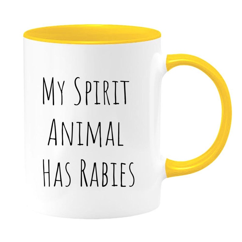 May include: White ceramic mug with a yellow rim and handle. The mug has black text that reads "My Spirit Animal Has Rabies."