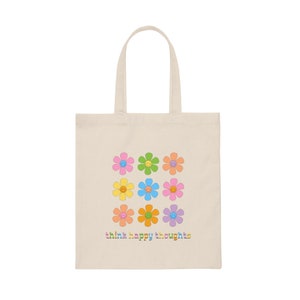 May include: A beige tote bag with a design of nine colorful flowers with smiley faces. The text "think happy thoughts" is printed in rainbow colors at the bottom of the bag.