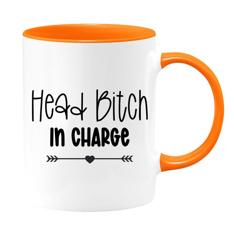 May include: White ceramic coffee mug with an orange rim and handle. The mug has black text that reads "Head Bitch in Charge" with a small black heart and arrows on either side.