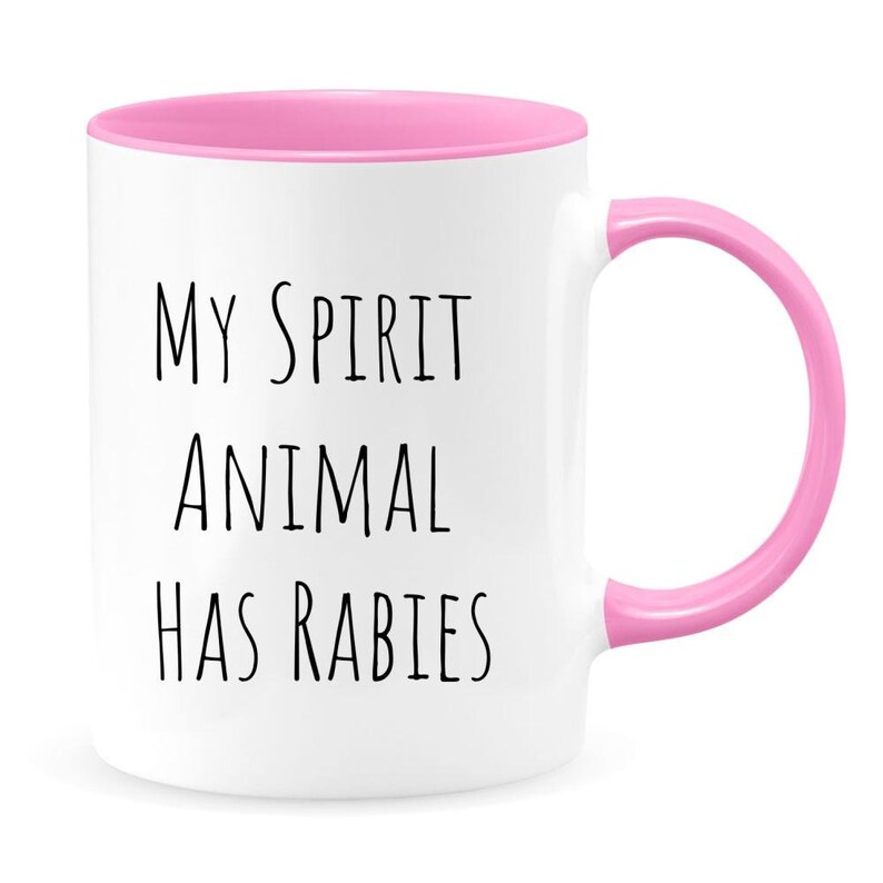 May include: White ceramic coffee mug with a pink rim and handle. The mug has black text that reads "My spirit animal has rabies".