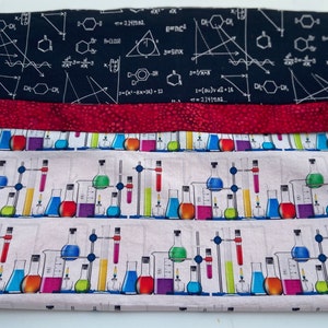 May include: A white fabric with a repeating pattern of colorful beakers and test tubes. The fabric has a red stripe and a black stripe with white mathematical equations and diagrams.