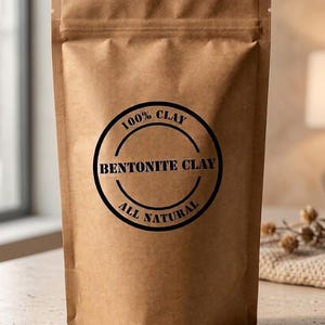 May include: A brown paper stand-up pouch containing bentonite clay. The front features a circular black label with the text 100% CLAY, BENTONITE CLAY, and ALL NATURAL printed in a bold, sans-serif font. The pouch has a sealed top edge.