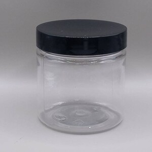 May include: A clear glass jar with a black lid. The jar is empty and has a smooth, rounded bottom.