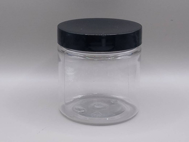 May include: A clear glass jar with a black lid. The jar is empty and has a smooth, rounded bottom.