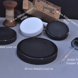 Könnte beinhalten: Sortiment an schwarzen und weißen geriffelten, ausgekleideten Deckeln für Gläser in verschiedenen Größen, darunter 58 mm, 70 mm und 89 mm. Ein Glas-Tropfer mit schwarzer Kappe ist ebenfalls enthalten.