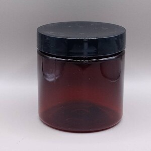 May include: A clear amber glass jar with a black lid. The jar is empty and has a smooth, rounded shape.