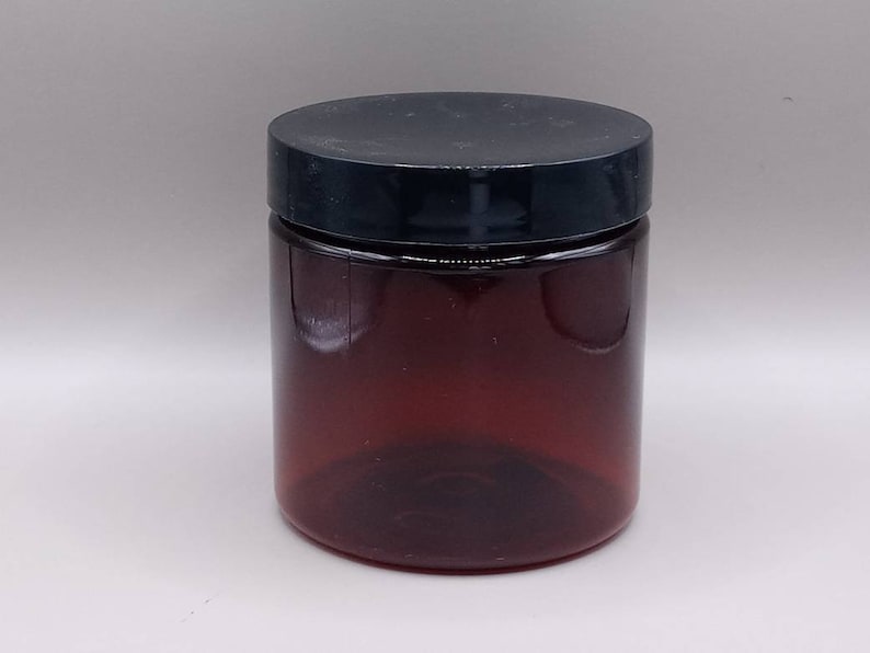 May include: A clear amber glass jar with a black lid. The jar is empty and has a smooth, rounded shape.
