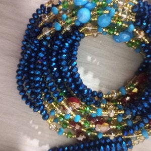 Puede incluir: Un collar de cuentas multicadena con cuentas azules, verdes, doradas y rojas. El collar est&aacute; hecho de cuentas de varios tama&ntilde;os y formas, incluyendo cuentas peque&ntilde;as redondas, cuentas facetadas m&aacute;s grandes y cuentas planas de forma ovalada.