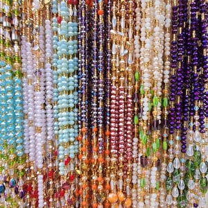 Puede incluir: Primer plano de una variedad de collares de cuentas de diferentes colores, incluyendo morado, azul, verde, blanco y naranja. Las cuentas est&aacute;n enhebradas en un alambre de color dorado.