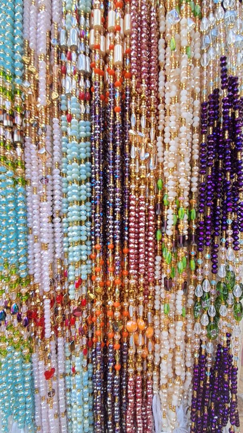 Puede incluir: Primer plano de una variedad de collares de cuentas de diferentes colores, incluyendo morado, azul, verde, blanco y naranja. Las cuentas est&aacute;n enhebradas en un alambre de color dorado.