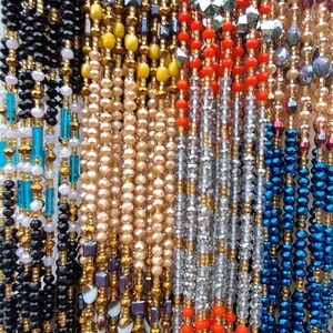 Puede incluir: Una colecci&oacute;n de collares de cuentas de varios colores, incluyendo negro, dorado, blanco, rojo, azul y turquesa. Las cuentas est&aacute;n dispuestas en filas verticales, creando un patr&oacute;n colorido y texturizado.